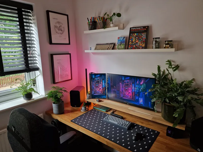 Wooden desk with computer screens, notebooks, and plants in a home office.